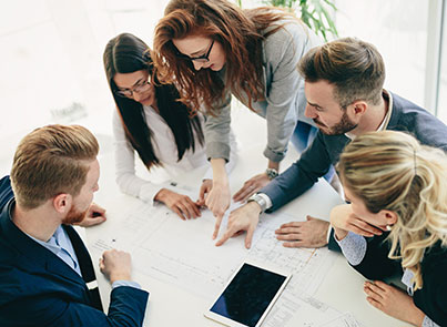 Group of business professionals huddled around a table, looking at a shared project